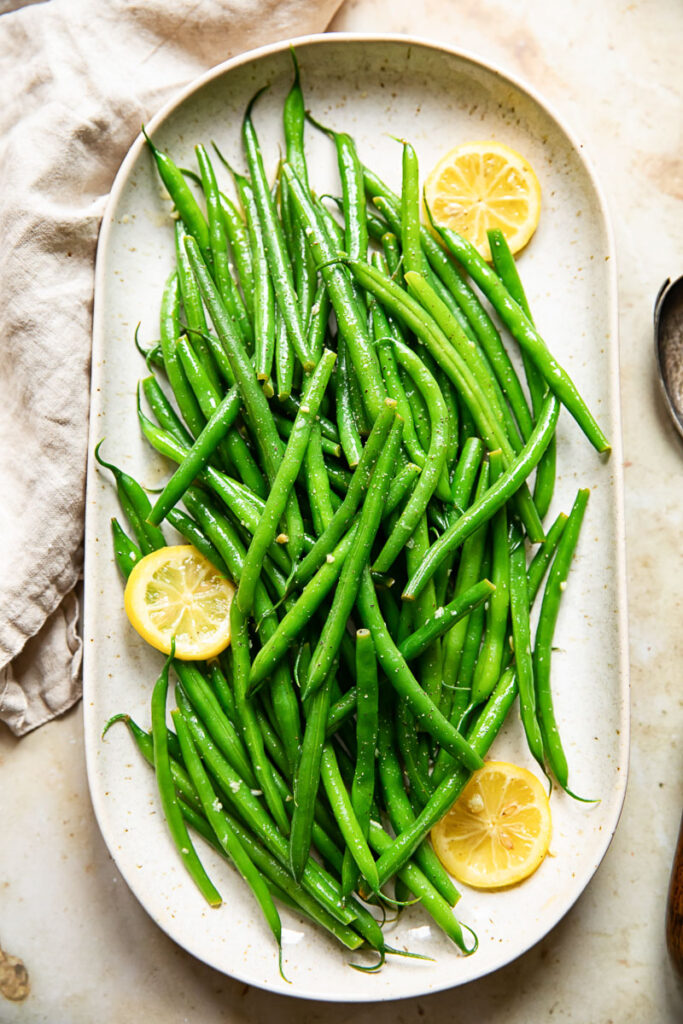 Platter of green beans with lemon butter, with visible lemon slices. 