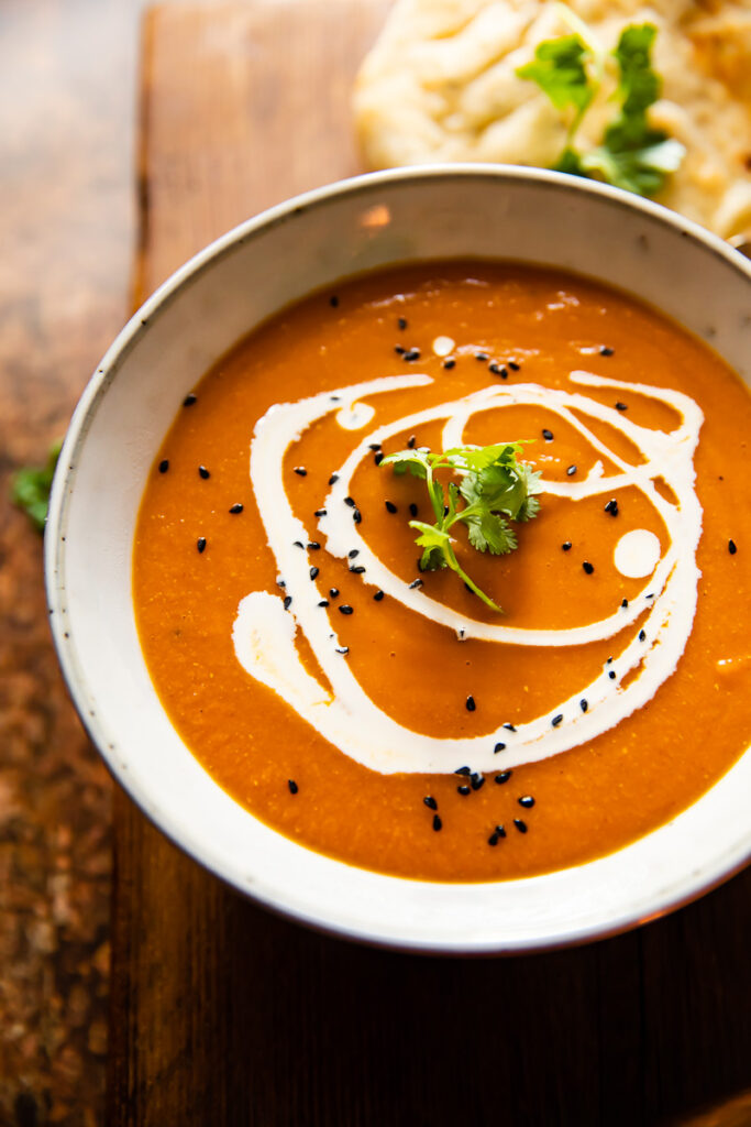 A bowl of spiced carrot and lentil soup on a wooden background