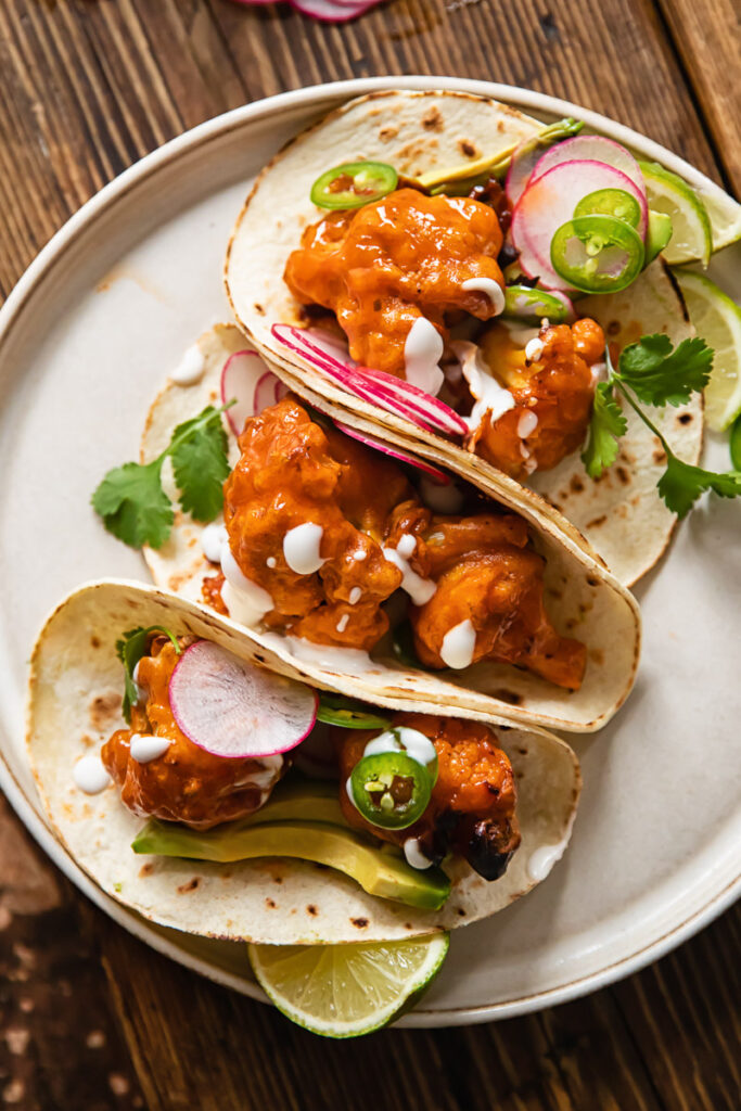 Buffalo cauliflower tacos folded and leaning together on a plate