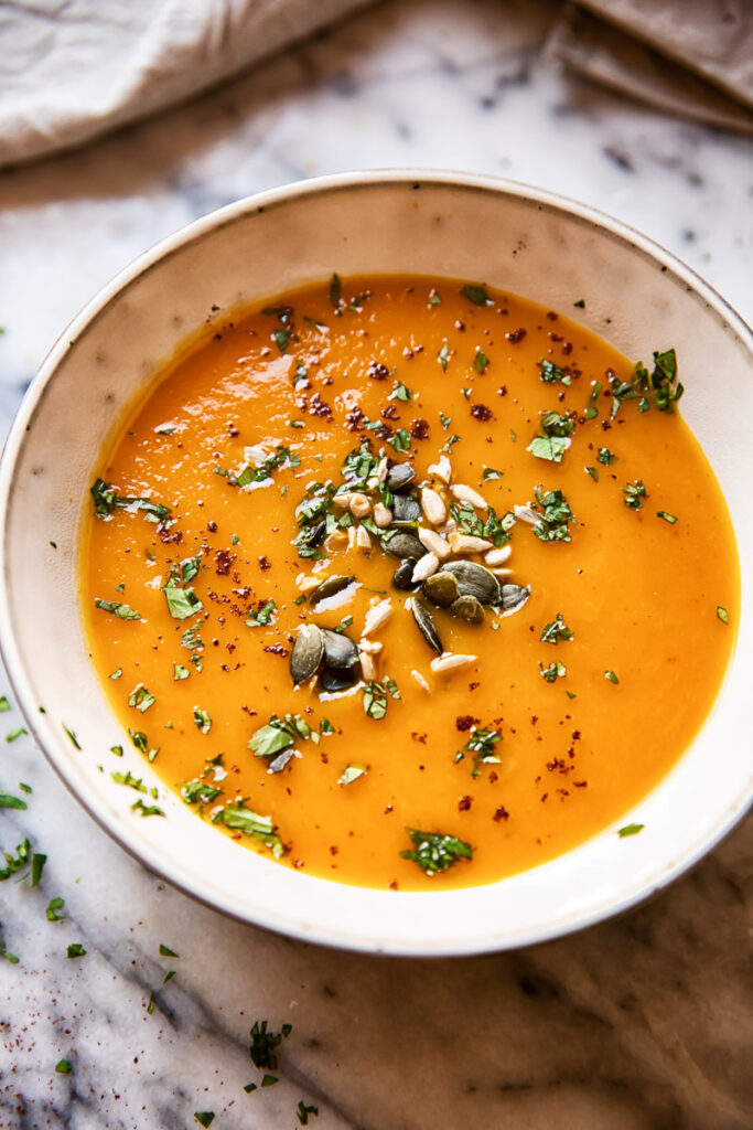 Bowl of sweet potato and carrot soup with seeds and herbs sprinkled on top