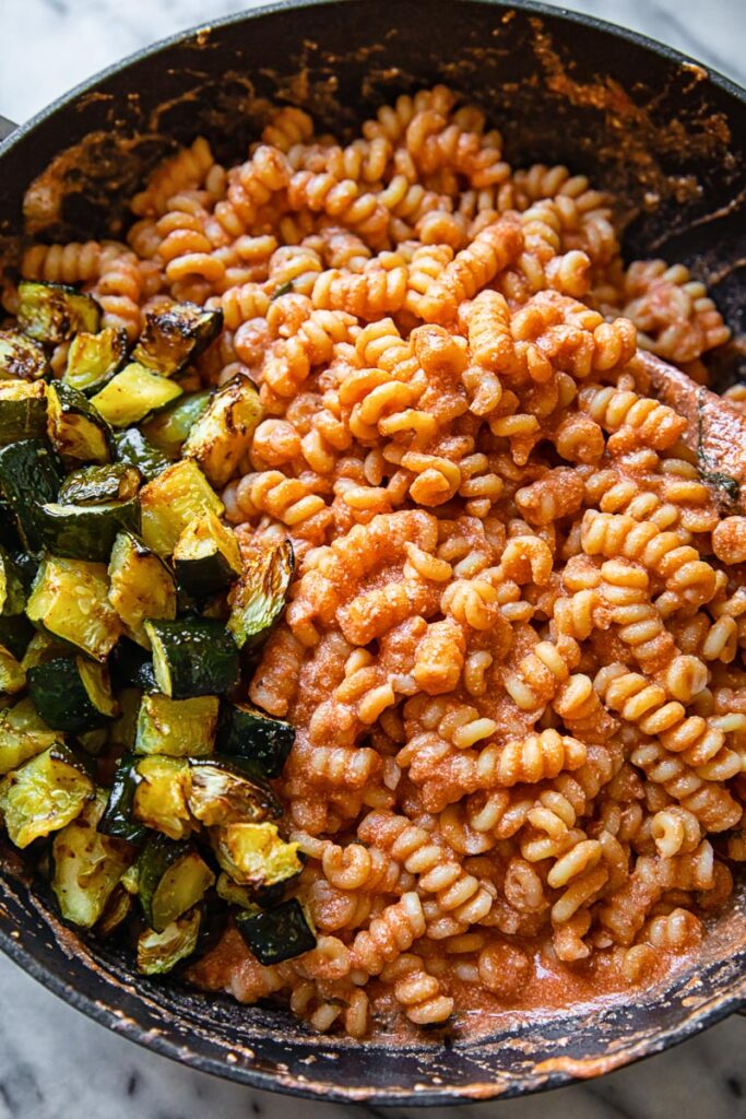 Pan with pasta covered in sauce and portion of fried zucchini