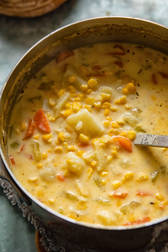 close up of a saucepan with corn chowder and a ladle